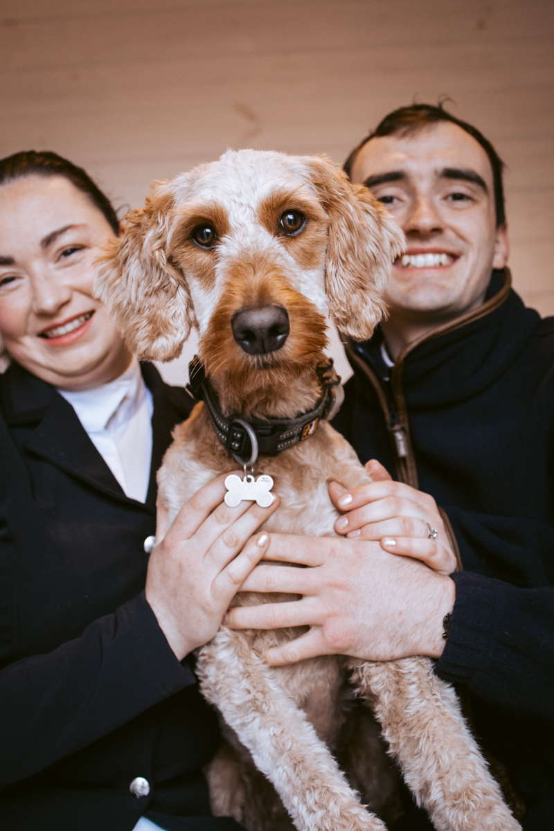 A woman and a man hold a dog between them, smiling and showcasing a joyful, affectionate moment.