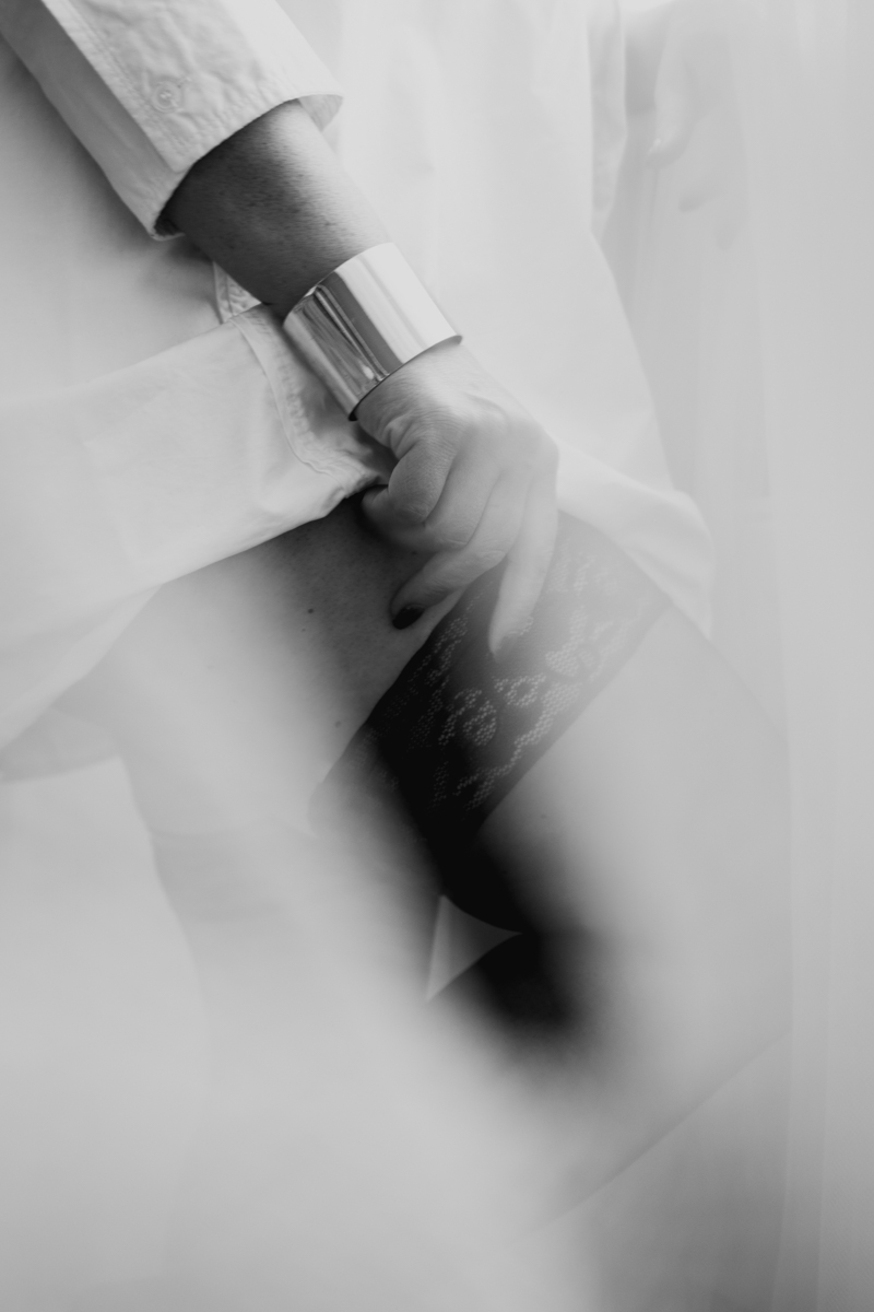 Close-up of a person's hand gripping a lace stocking, wearing a silver cuff bracelet, partially obscured by soft fabric.