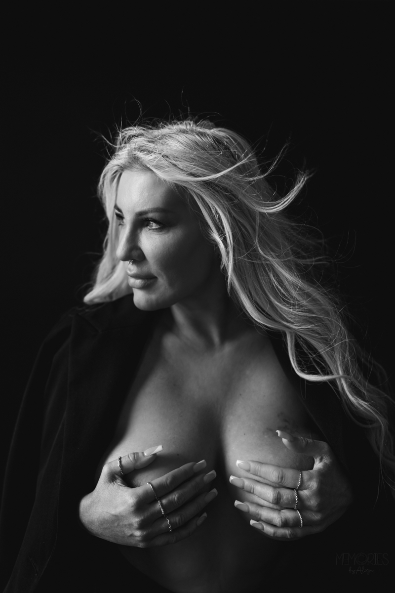 A black and white portrait of a woman with long flowing hair, looking confidently to the side while holding her hands around her upper body.