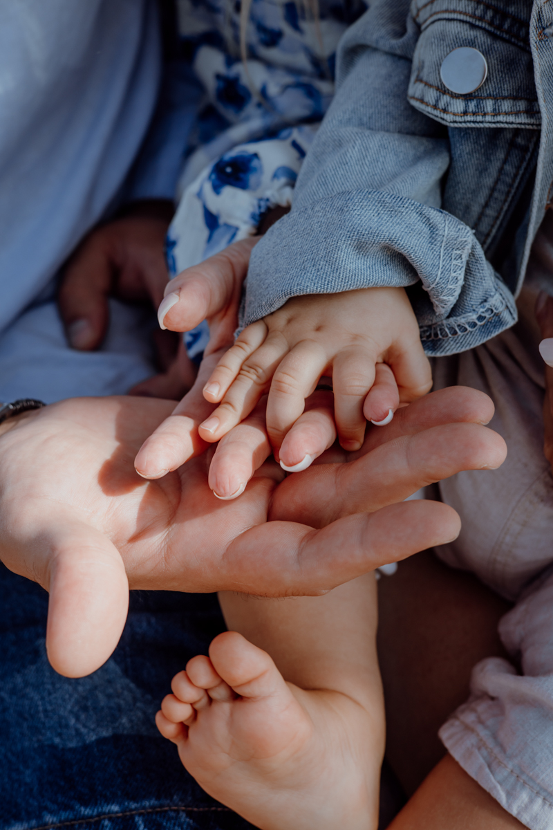 A close-up image of hands, featuring an adult hand and a child's hand gently placed together, along with a small child's foot visible in the foreground.