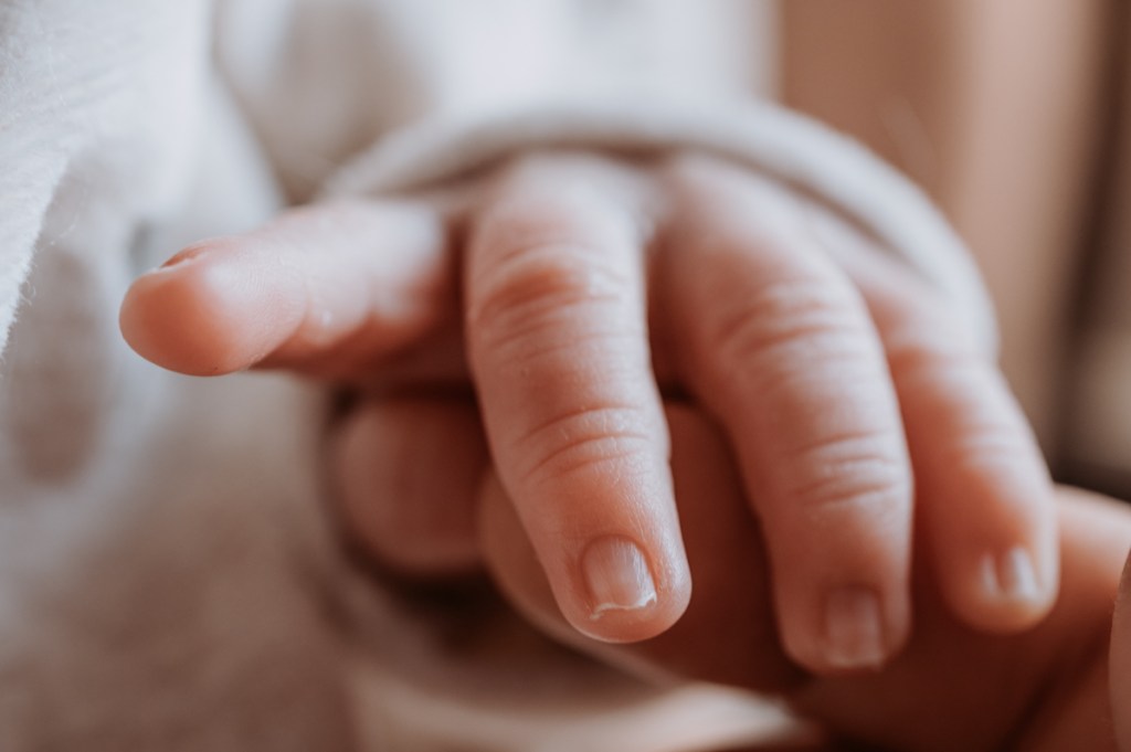 Close-up of a small hand reaching out to touch a larger hand, showcasing delicate fingers and skin texture.