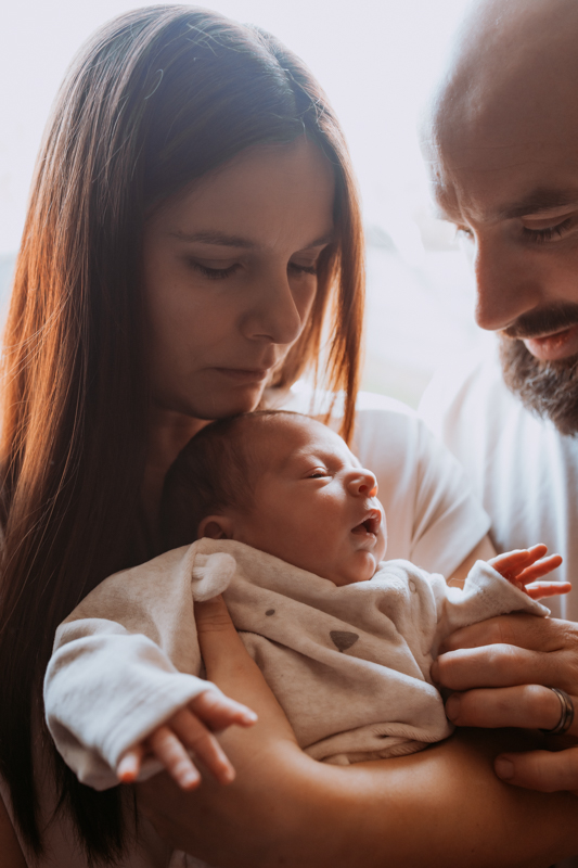 A mother and father holding their newborn baby, with tender expressions as they gaze at their child.